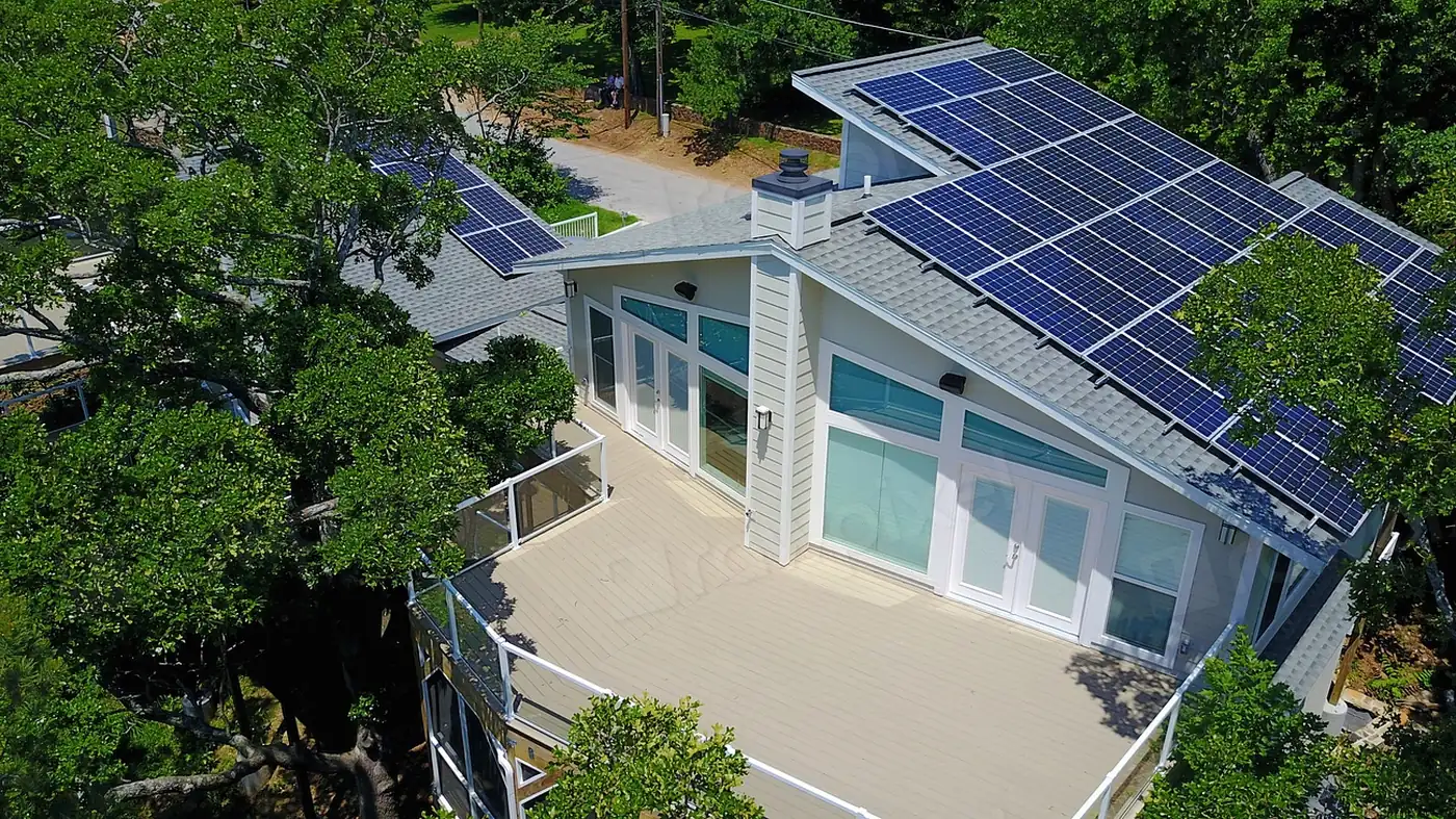 Aerial view of a house with rooftop solar panels surrounded by trees